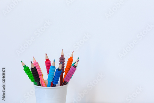 Colored pencils in white cup against white wall with copy space