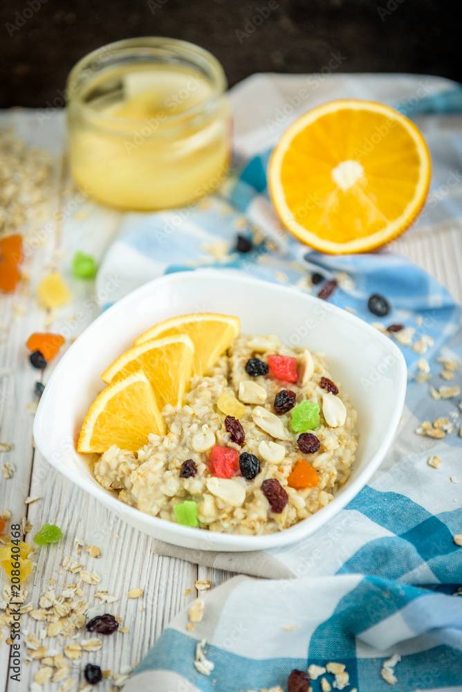 Homemade oatmeal porridge with honey, orange, raisin, peanut and candied fruit on white wooden background. Healthy breakfast. Homemade oatmeal porridge with honey, orange, raisin, peanut and candied fruit on white wooden background. Healthy breakfast.