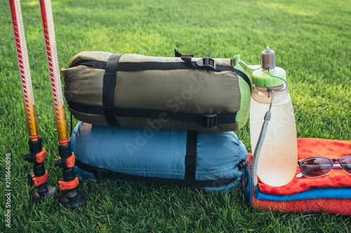 sleeping bags, trekking poles, water and other things for travel on a green grass