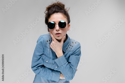 Young brunette girl in round glasses. Hairs are gathered in a bun. The girl put her hand to her chin. photo