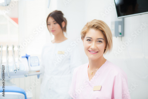 A blond dentist girl in a treatment room  on the background of another dentist girl