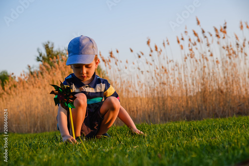 Boy child playing with windmill in green grass of the beach on summer vacation concept for freedom