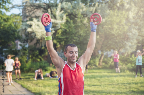 Young athlete performs exercises with dumbbells in the fresh air.