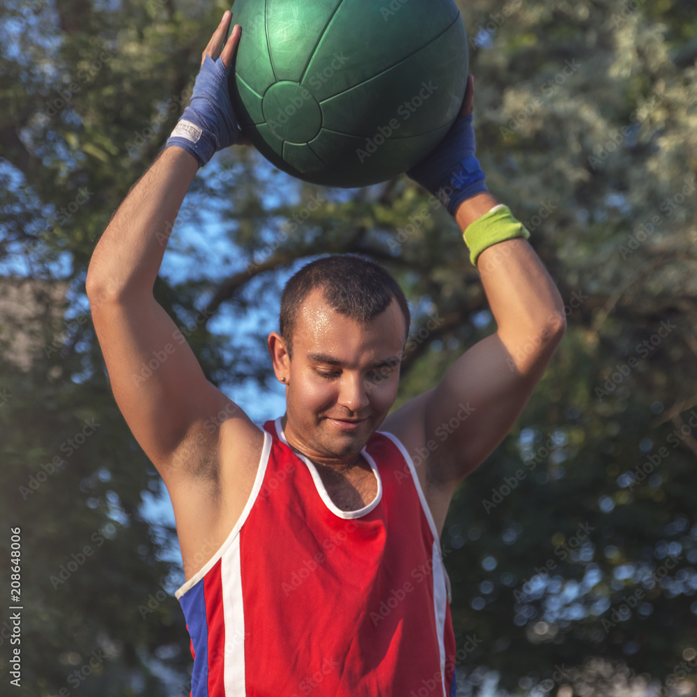 Young athlete performs sports exercises with a ball outdoors.