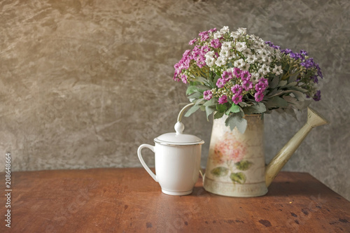 Flower bouquet in white water can and white coffee cup place on wood desk with Polished cement wall.Retro design image.