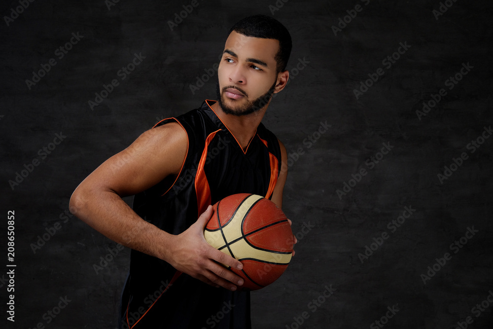 Young African-American basketball player in sportswear isolated over dark background. Young African-American basketball player in sportswear isolated over dark background.