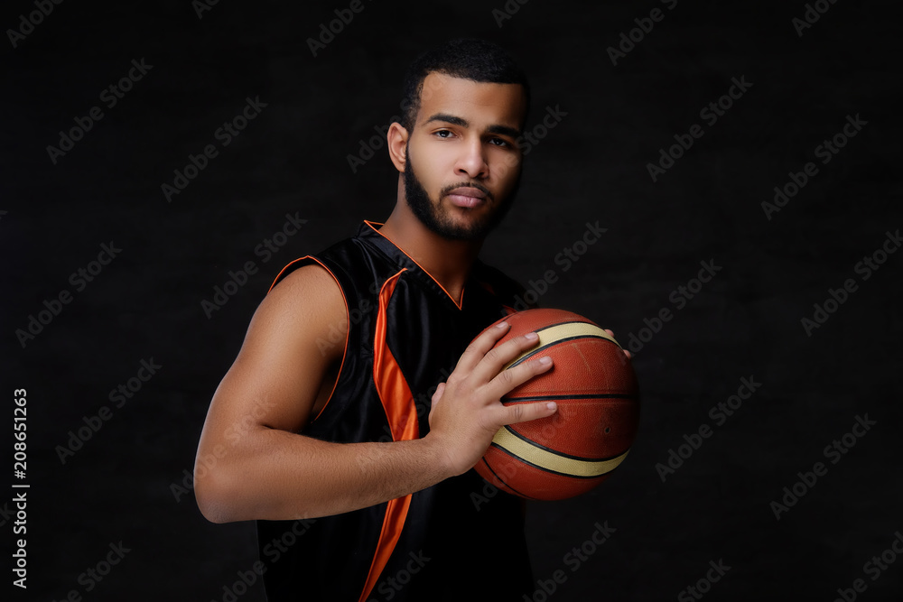 Naklejka premium Young African-American basketball player in sportswear isolated over dark background.