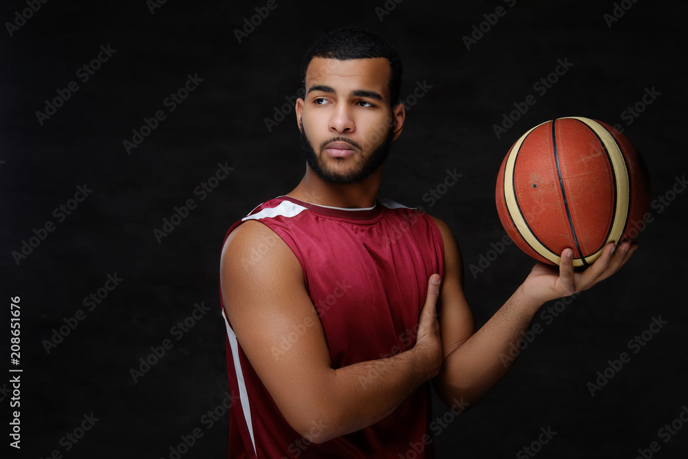 Young African-American basketball player in sportswear isolated over dark background. Young African-American basketball player in sportswear isolated over dark background.