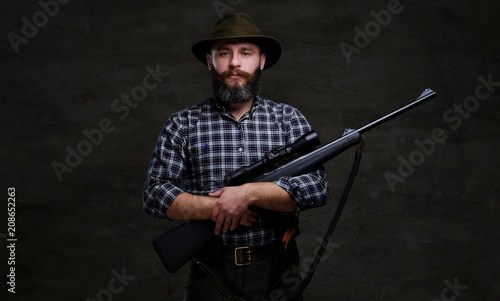Handsome bearded hunter traveler in a fleece shirt and hat holds rifle with a sight. 