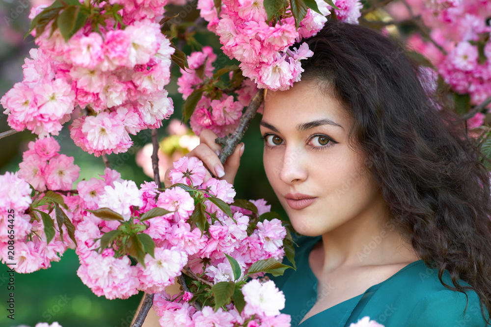 Fototapeta premium beautiful girl posing near pink sakura flowers as background, face closeup, spring landscape