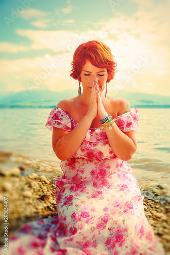 beautiful girl with radiant red hair in sommer dress in a meditative spiritual gesture of prayer.