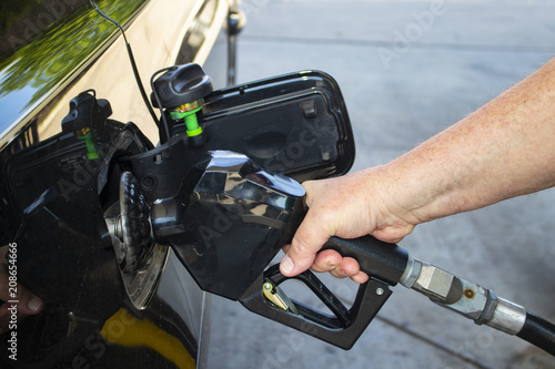Man's hand holding nozzle of gas pump and putting gas into black car