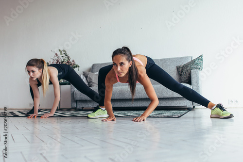 Two fit girls doing home workout performing lateral lunges at home.