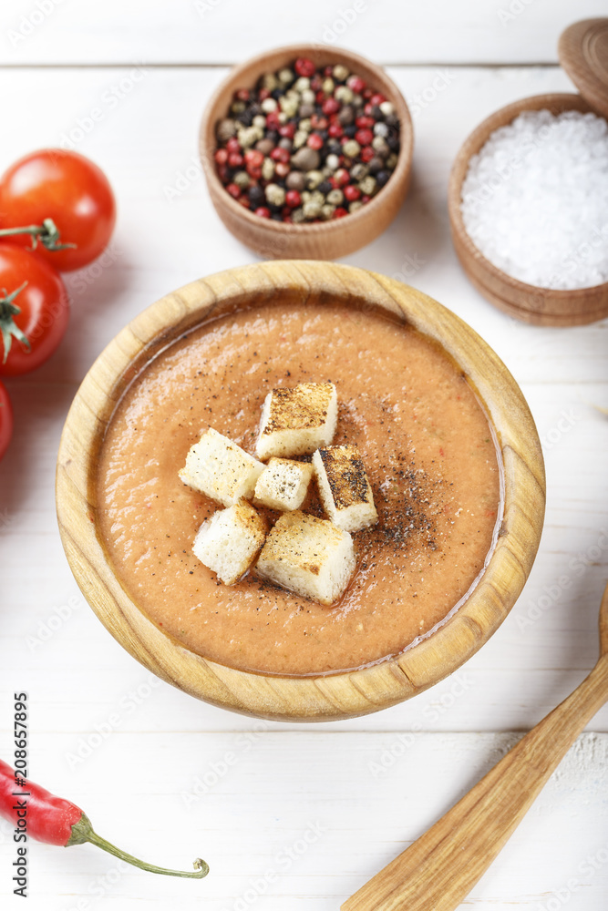 soup gazpacho with crackers, in a wooden plate, on a white wooden background.