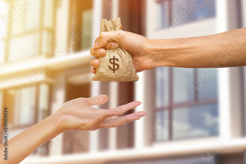 A man hand holding a money giving to another person for buying real estate. Loans for real estate concept. Conceptual give money to someone else to exchange real estate.