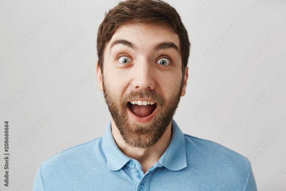 Happiest man on earth. Studio shot of excited and surprised caucasian guy smiling broadly and staring with popped eyes at camera, being thrilled to receive awesome news, posing over gray background Happiest man on earth. Studio shot of excited and surprised caucasian guy smiling broadly and staring with popped eyes at camera, being thrilled to receive awesome news, posing over gray background