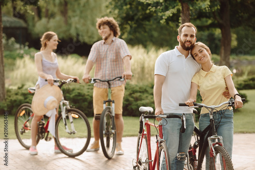 Young couple of cyclists is hugging. Beautiful young couple in love walking with bicycles. Active summer holiday.