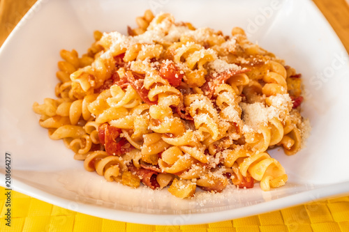 Pasta spirals with salami and tomato in a white dish on a yellow place mat