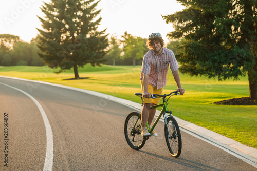 Attractive young man enjoying riding his bicycle. Cheerful guy riding bicycle on the road. Active summer holiday concept.
