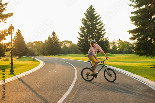 Male student enjoying riding bike. Young cheerful man cycling on country road, sunny day. People and healthy lifestyle.
