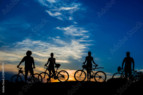 Silhouettes of cyclist on beautiful evening sky background. Group of friends with bikes on sunset sky background. Enjoying of beauty.