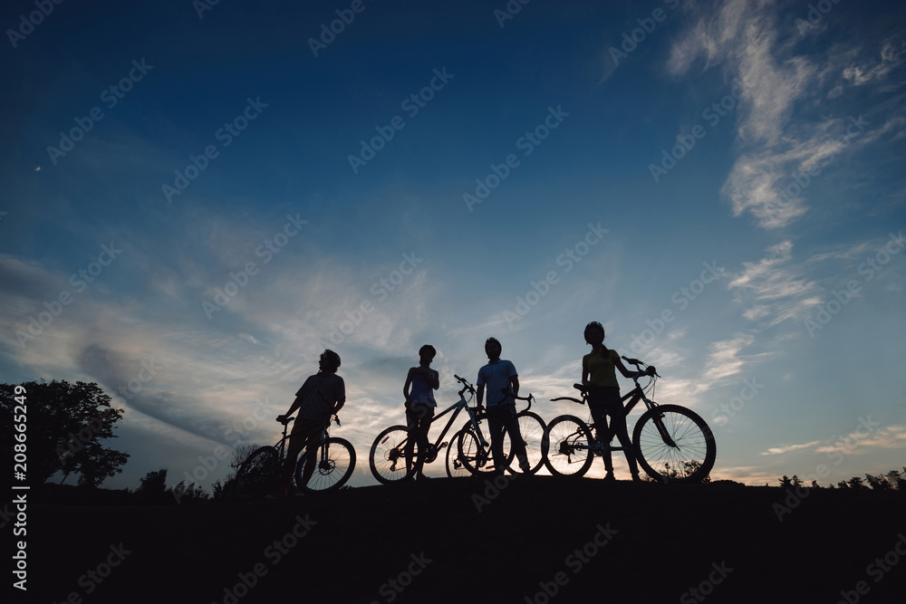 Naklejka premium Cyclists on hill at sunset sky. Silhouettes of bikers on evening sky background. Amazing rest ever.