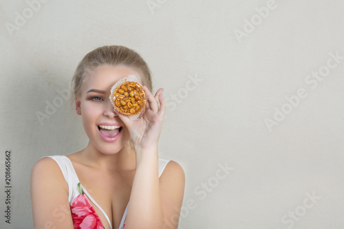 Joyful blonde girl having fun with cupcake in hand and covering her eye. Bakery and sweets concept. Space for text
