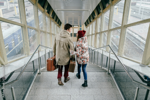 Lifestyle couple of young happy lovers carry vintage brown suitcases at railway station. Pair of stylish cheerful hipsters going down the stairs.  Handsome man travel with his lovely girlfriend.