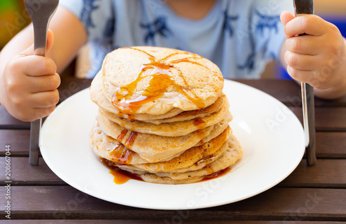Hungry small child sitting in front of a vegan buckwheat pancake tower with maple syrup