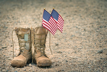 Old military combat boots with dog tags and two small American flags. Rocky gravel background with copy space. Memorial Day or Veterans day concept.