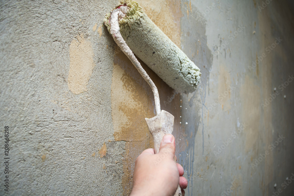 Close-up hand holds rolling paint brush, painting interior stucco wall with  white color.Preparation of walls for painting or wallpapering, priming with  a roller Stock Photo | Adobe Stock