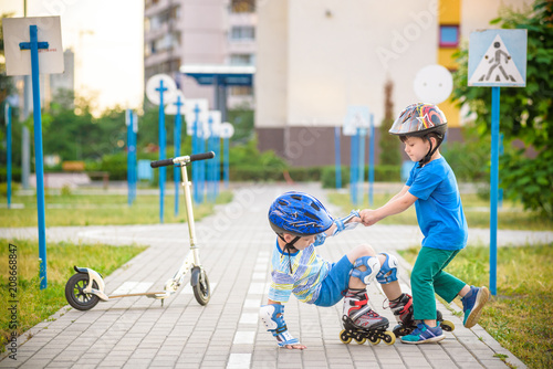 two boys in park, help boy with roller skates to stand up