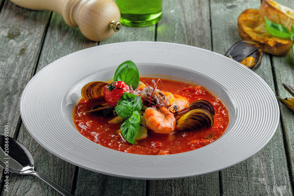 Excellent soup made of tomato and seafood on a rustic wooden table. Plate of healthy Italian meal.