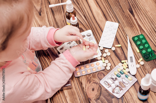 Children's hands with medicines on a wooden table. A small child left unattended plays dangerous drugs