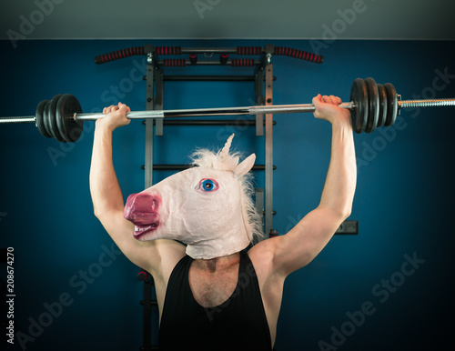 Funny man in comical mask doing sport exercise. Unusual guy pump up iron at home. Unicorn sportsman. photo