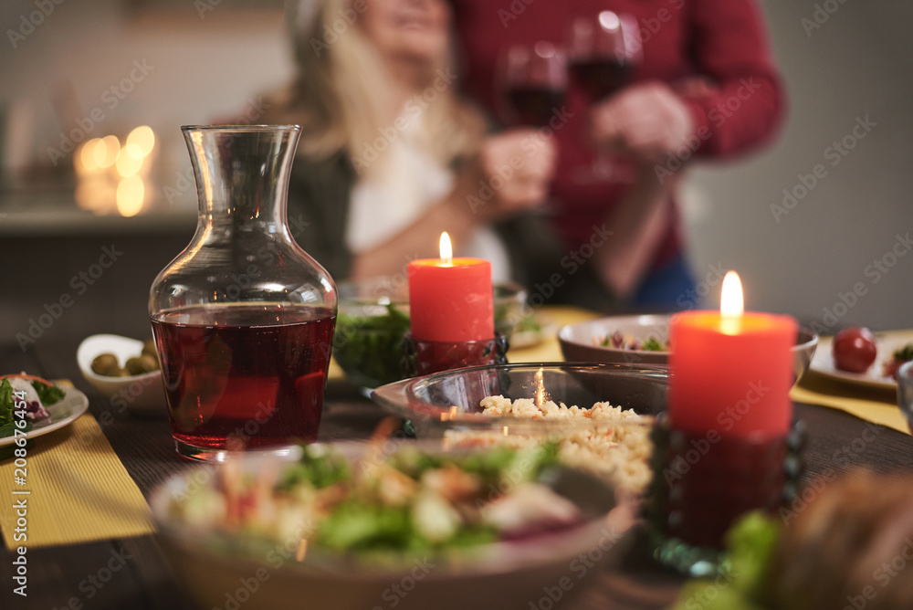 Focus of candles lit on festive dinner. There are red wine and variable dishes on table creating romantic atmosphere for couple on background 
