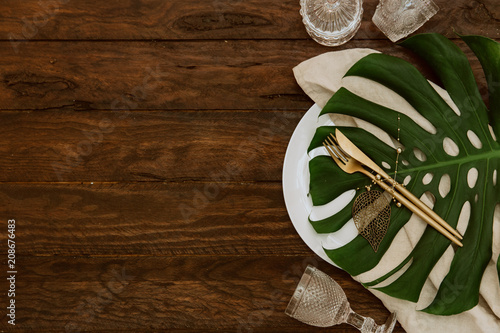 Fototapeta Naklejka Na Ścianę i Meble -  Gold cutlery with linen napkin and monstera leaf on wooden background. Wedding festive tableware