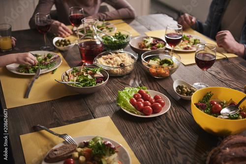 Close up of healthy dishes lying on wooden board. Family sitting together and eating vegetables  salads  rice  tomatoes  and drinking red wine