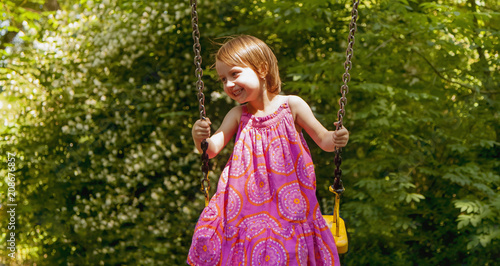 Cute little child girl having fun on a swing on summer day. Happy childhood concept.