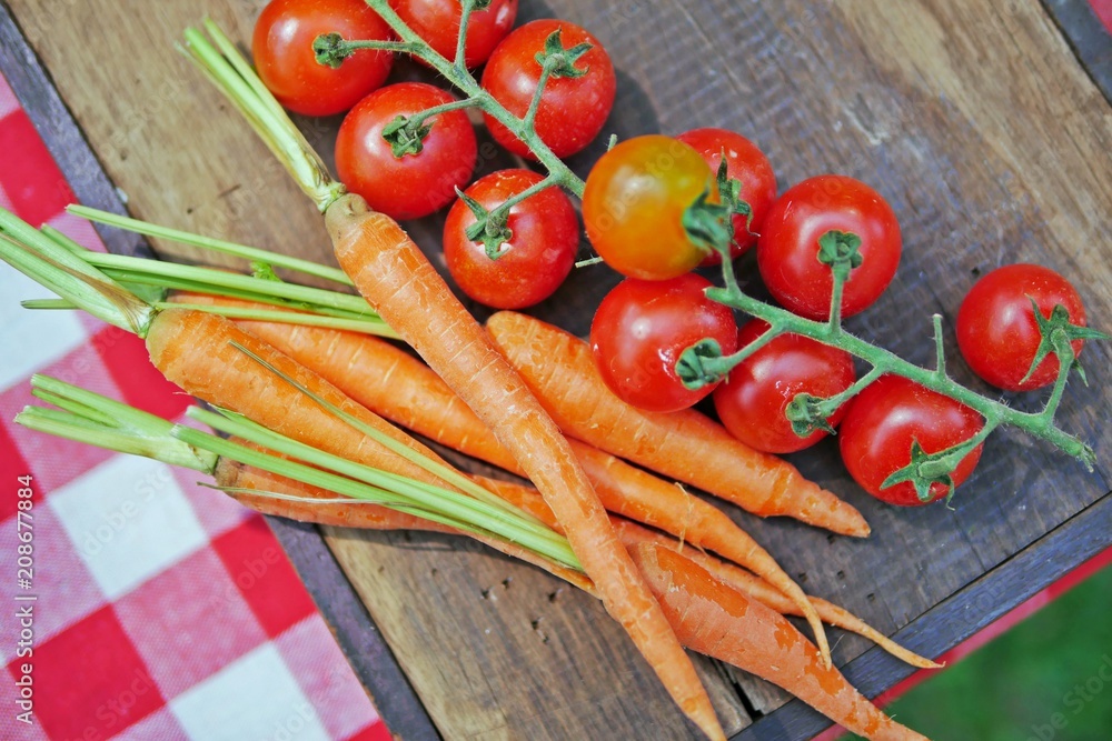 Fresh, raw vegetables for cooking:carrots and red vine-ripened cherry tomatoes on a wooden cutting board. Top view. Fresh, raw vegetables for cooking:carrots and red vine-ripened cherry tomatoes on a wooden cutting board. Top view.