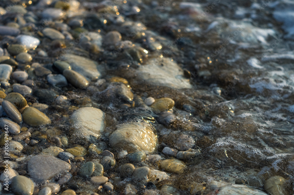 pebble stones on the sea beach, the rolling waves of the sea with foam