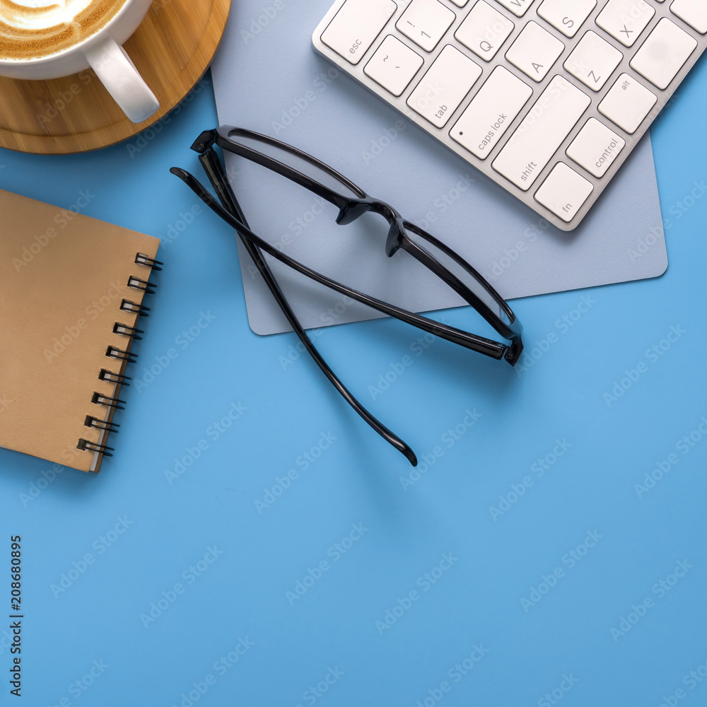 Flat lay, top view office table desk. Workspace with blank note book, keyboard, office supplies and coffee cup on light blue background. Flat lay, top view office table desk. Workspace with blank note book, keyboard, office supplies and coffee cup on light blue background.