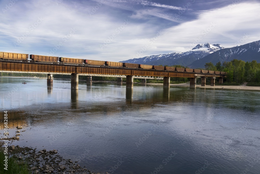 Landscape View of Freight Train Crossing Railway Bridge over Columbia River in Revelstoke, British Columbia Canada