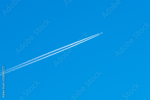 The aircraft in the blue sky. The airplane leaves behind a white condensation trail or inversion trail. Travel concept