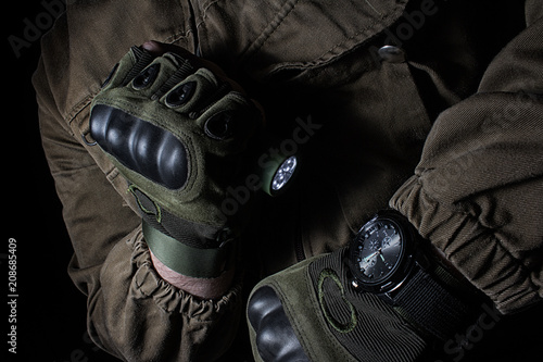 Foto Photo of a male person in brown tactical outfit jacket and gloves using green tactical led flashlight and military watch