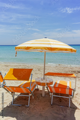 Beach equipment  chairs and sun umbrella on white sandy beach with light blue sea water  beach vacation concept