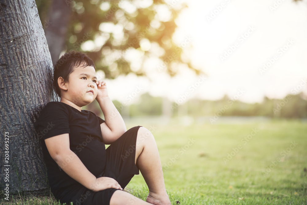 Little boy sitting under the tree thinking something Little boy sitting under the tree thinking something