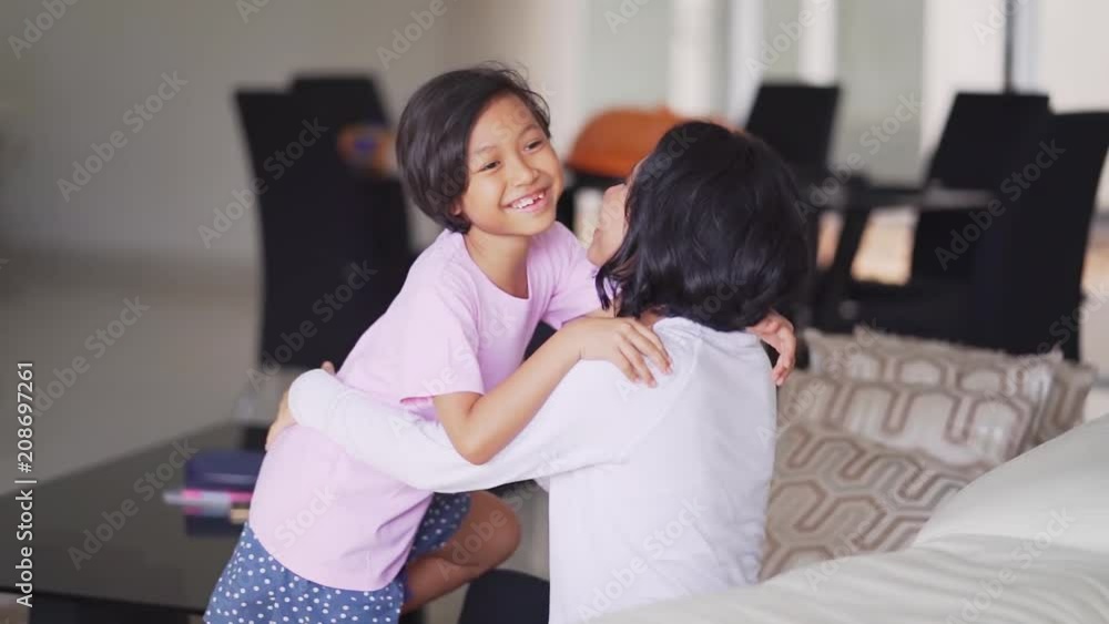 Slow motion of cheerful little girl hugging her mother on the sofa in the living room at home Slow motion of cheerful little girl hugging her mother on the sofa in the living room at home