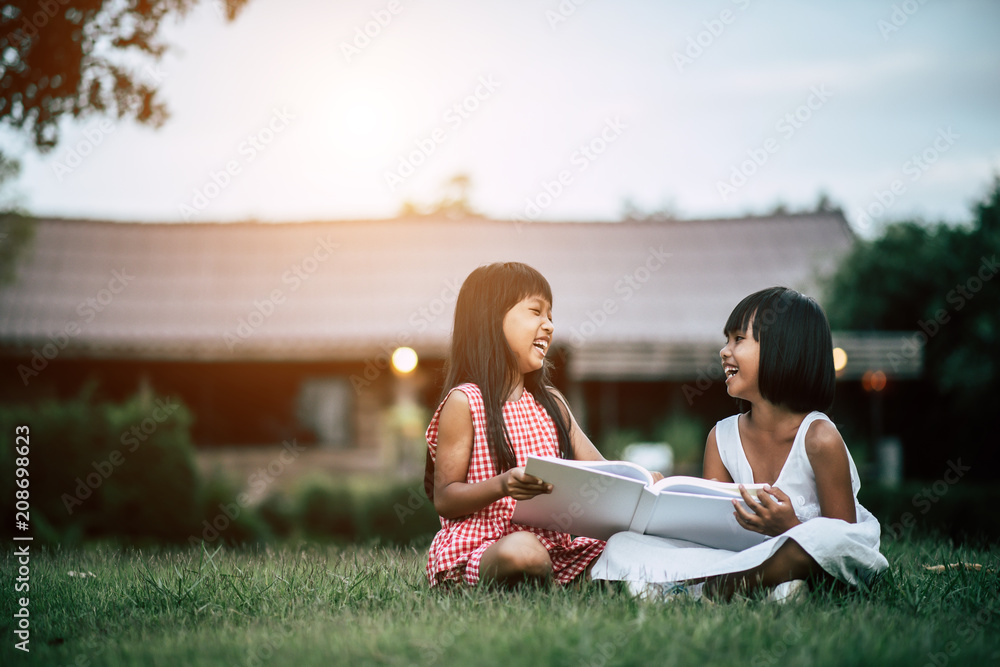 Two little girl friends in the park on the grass reading a book and learn