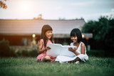 Two little girl friends in the park on the grass reading a book and learn